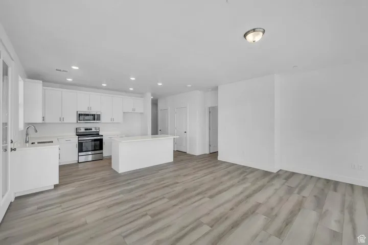 Kitchen featuring appliances with stainless steel finishes, light countertops, a kitchen island, white cabinets, and light wood finished floors