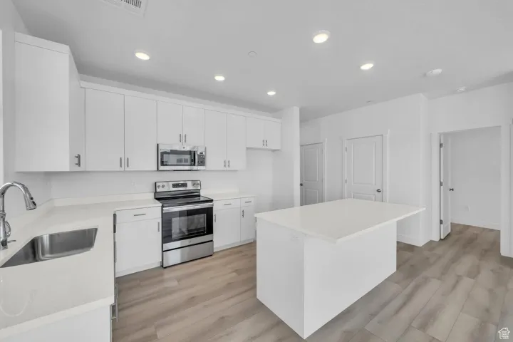 Kitchen featuring appliances with stainless steel finishes, recessed lighting, light countertops, white cabinets, and light wood-style floors
