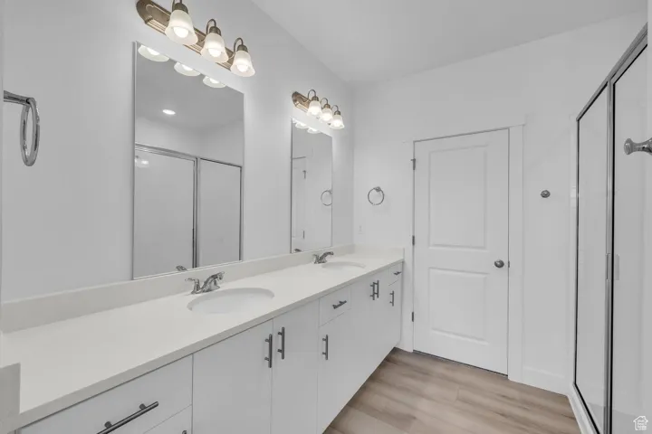 Bathroom with a shower stall, double vanity, and wood finished floors
