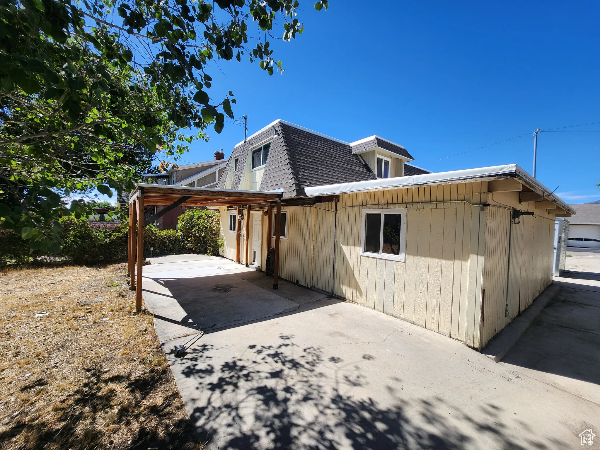 View of home's exterior with roof with shingles, mansard roof, a patio area, and driveway