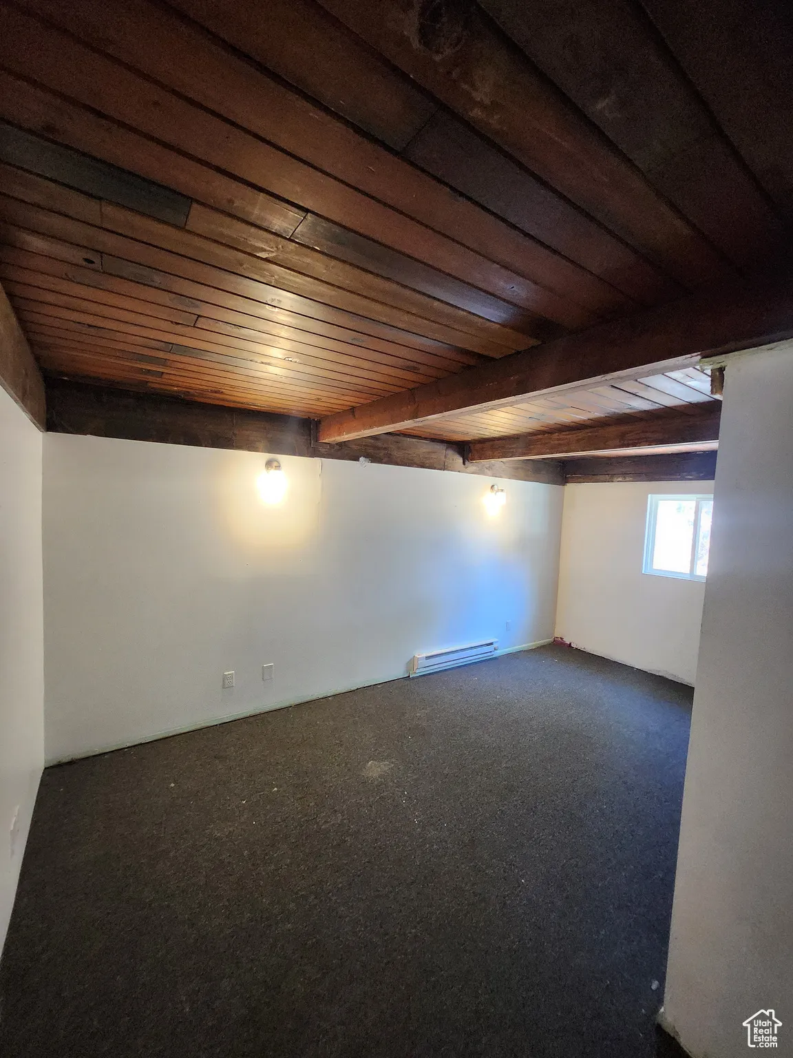 Carpeted spare room featuring a wood ceiling with exposed beams and baseboard heating