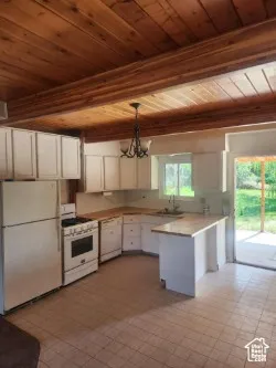 Kitchen with white appliances, decorative light fixtures, a wood ceiling with exposed beams, a chandelier, and white cabinets