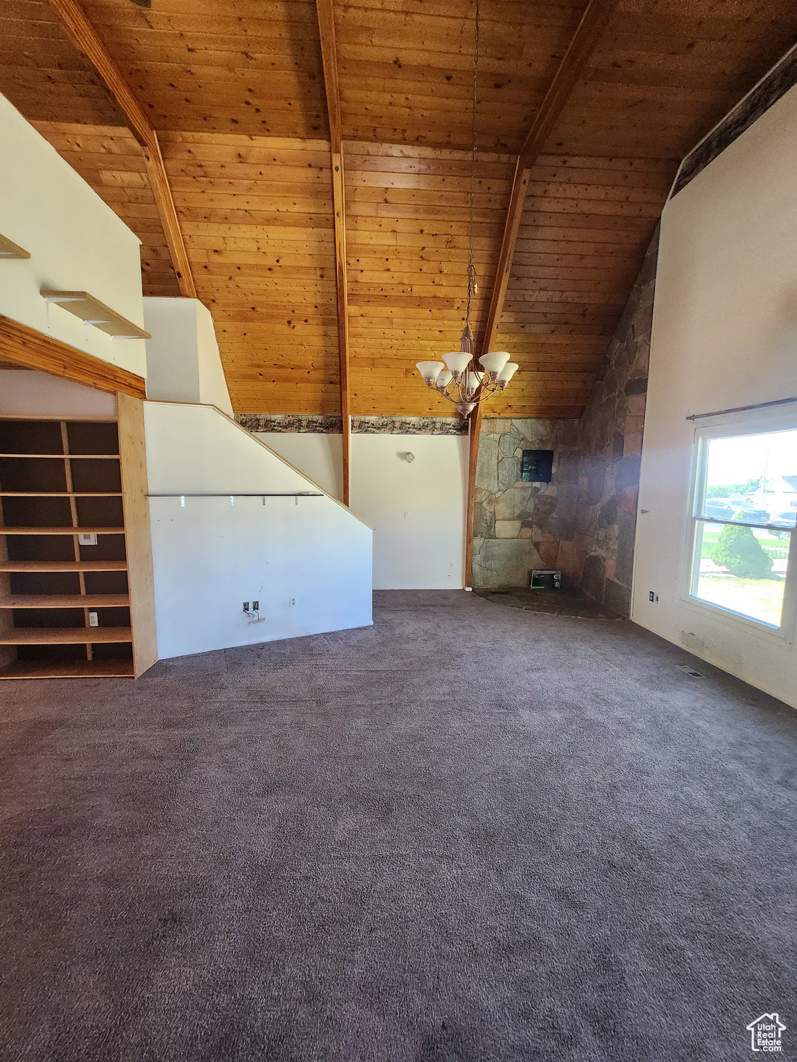 Unfurnished living room featuring high vaulted ceiling, a wood ceiling with exposed beams, a chandelier, and carpet