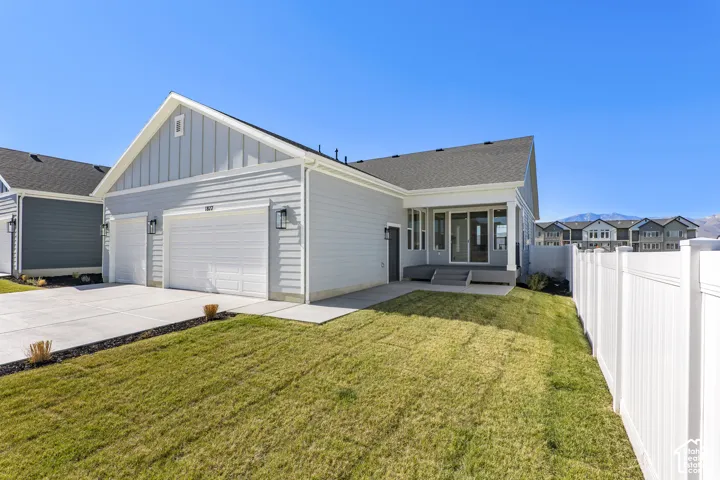 View of front facade with board and batten siding, driveway, an attached garage, a fenced backyard, and a patio area