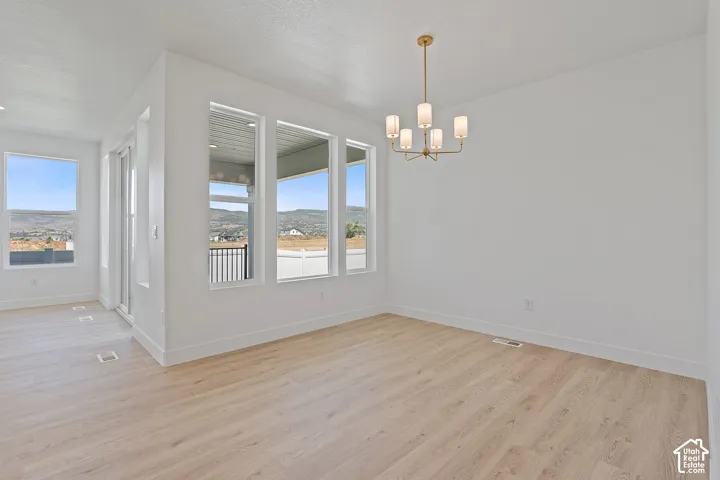 Unfurnished dining area featuring plenty of natural light, light wood-type flooring, a chandelier, and a textured ceiling