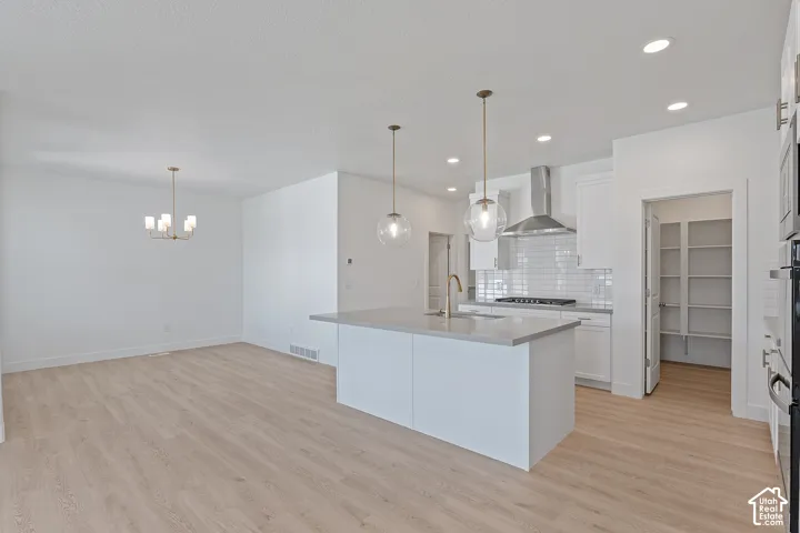 Kitchen with backsplash, white cabinets, light wood finished floors, wall chimney exhaust hood, and light countertops