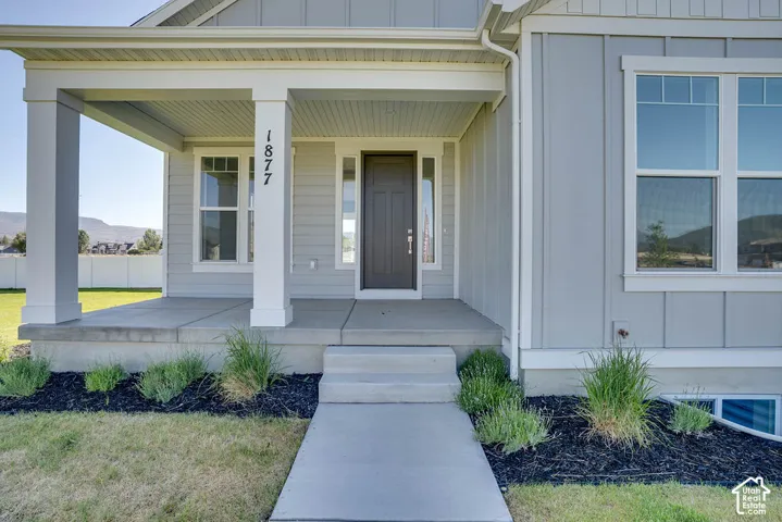 Welcoming concrete porch with two white square columns, light gray vertical siding, a dark entry door with a sidelight, and a white-framed window