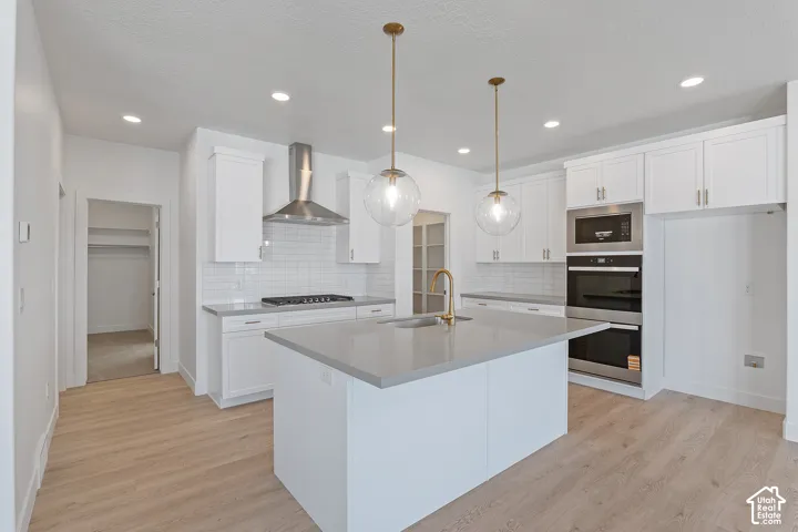 Kitchen with white cabinetry, stainless steel appliances, an island with sink, wall chimney range hood, and recessed lighting