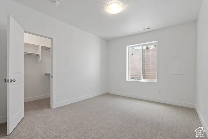 Unfurnished bedroom with light carpet, a spacious closet, and a textured ceiling