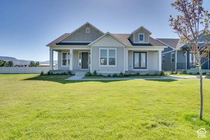 Light gray siding exterior with white trim, a covered front porch, an expansive green lawn, a white privacy fence, and a distant mountain backdrop