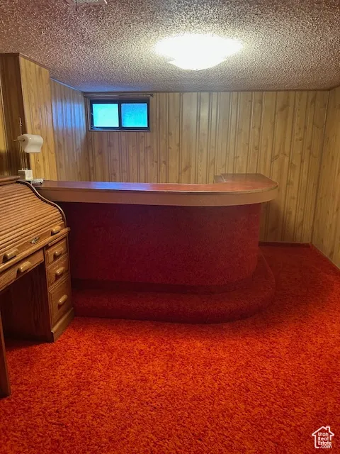 Unfurnished office with wooden walls, dark carpet, and a textured ceiling
