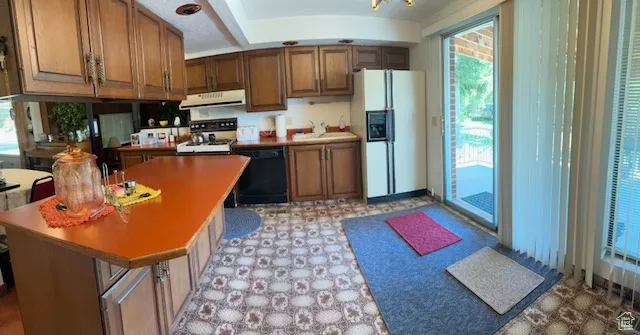 Kitchen with light flooring, white refrigerator with ice dispenser, brown cabinets, range, and black dishwasher