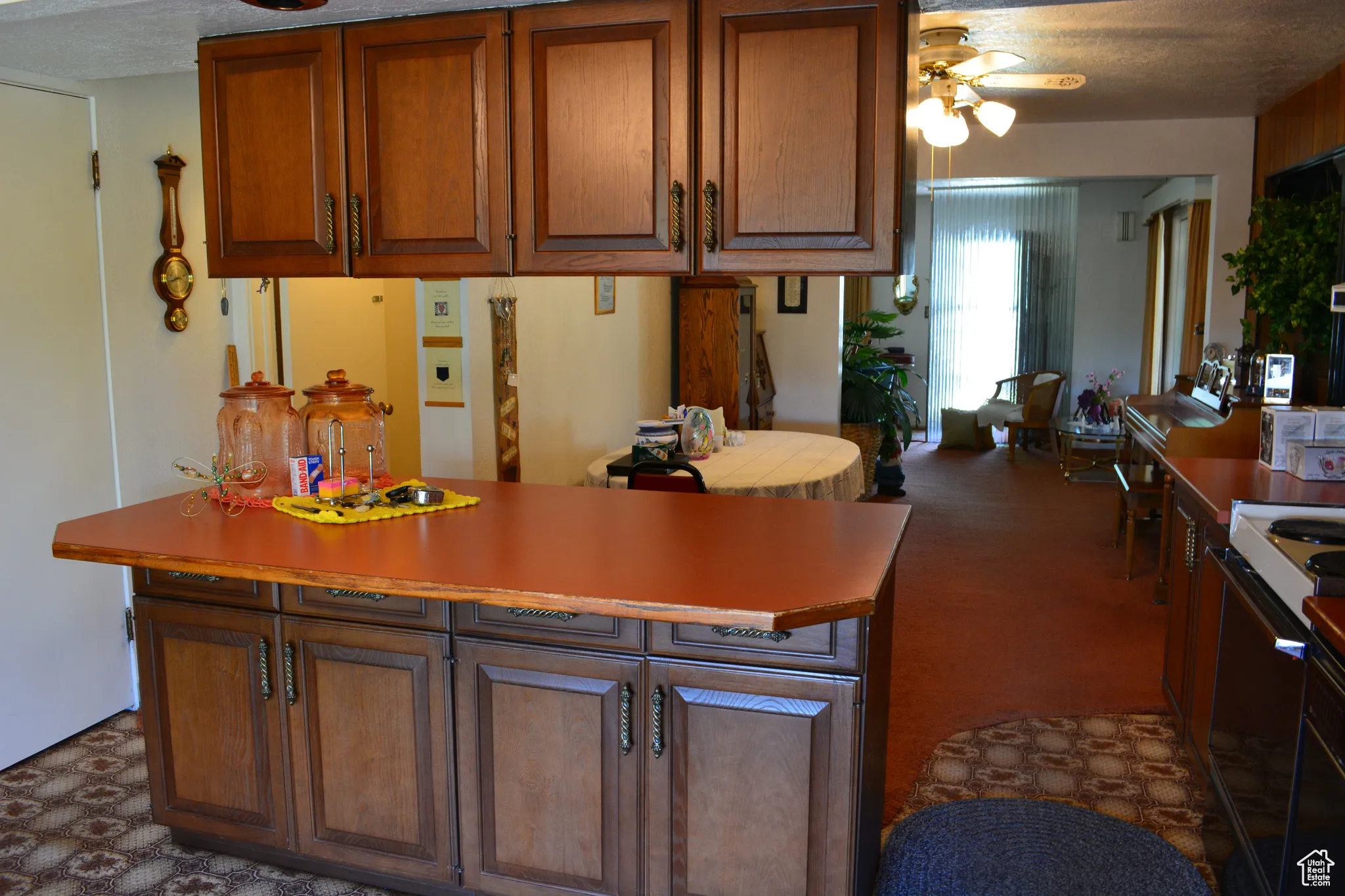 Kitchen with a ceiling fan, range, brown cabinets, a textured ceiling, and light countertops