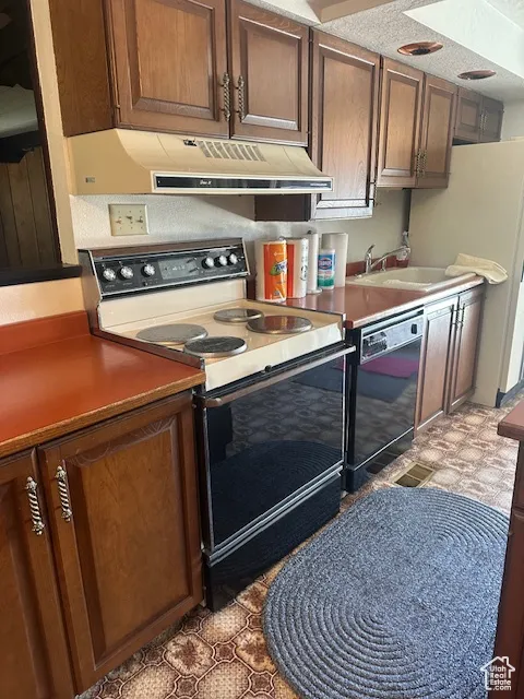 Kitchen with electric stove, freestanding refrigerator, under cabinet range hood, dishwasher, and brown cabinets