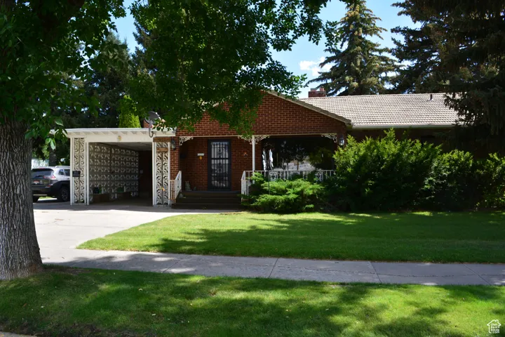 Single story home featuring a carport, driveway, a front lawn, stone siding, and a chimney