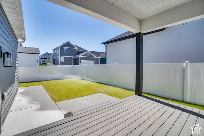 Covered deck with composite decking, featuring a white vinyl privacy fence, a manicured lawn, and concrete patio areas