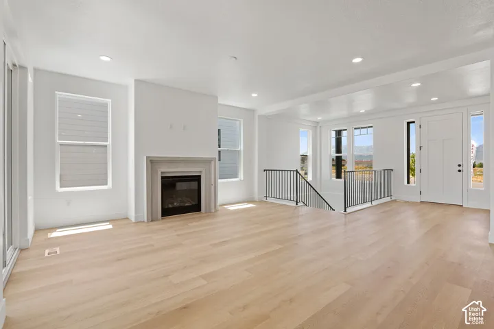 Unfurnished living room with light wood-style flooring, a glass covered fireplace, and recessed lighting
