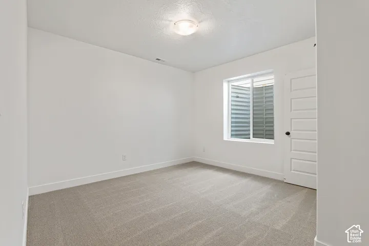 Empty room with light colored carpet and a textured ceiling