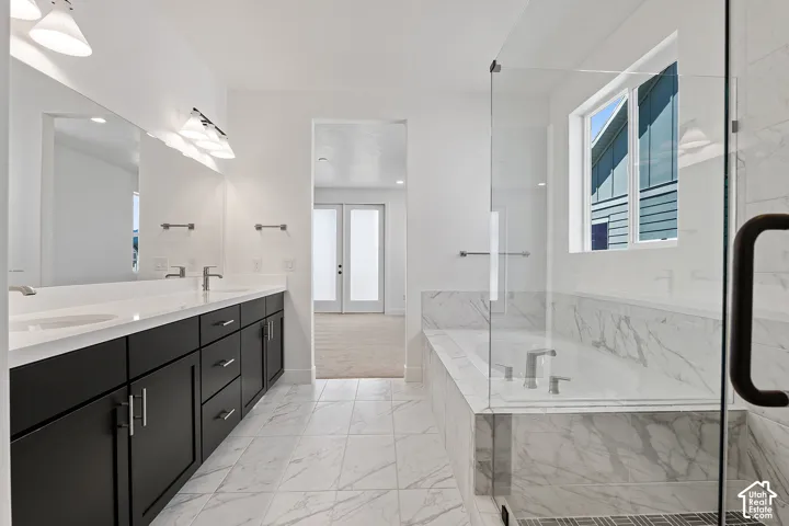 Bathroom featuring french doors, double vanity, a bath, and healthy amount of natural light