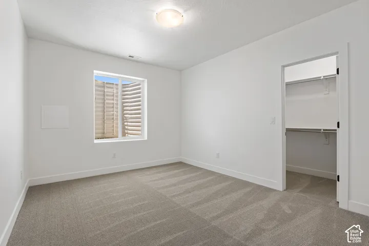 Unfurnished bedroom featuring carpet flooring, a walk in closet, and a textured ceiling