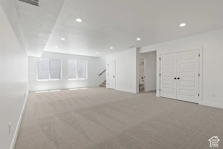Basement featuring light colored carpet, a textured ceiling, recessed lighting, and stairway