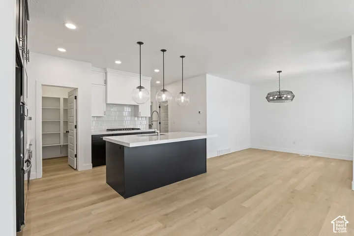Kitchen featuring tasteful backsplash, light countertops, white cabinets, recessed lighting, and an island with sink