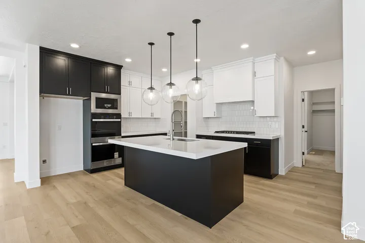 Kitchen featuring light countertops, dark cabinetry, light wood finished floors, a kitchen island with sink, and recessed lighting