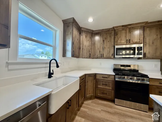 Kitchen featuring wood-finish cabinetry, white countertops, stainless steel appliances, a farmhouse sink with a matte black faucet, and wood-finish flooring