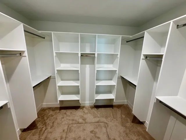 Walk-in closet featuring built-in white shelving, multiple hanging rods, and plush brown carpeting