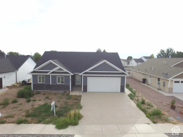 Modern ranch-style home featuring gray siding, dark stone accents, white trim, and a dark shingled roof