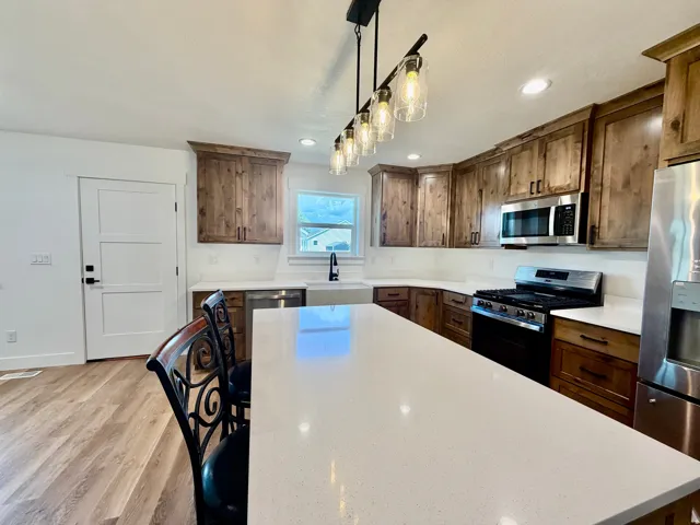 Spacious kitchen featuring a large island with white countertops, wood-finish cabinetry, stainless steel appliances, and wood-finish flooring