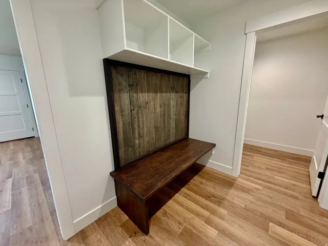 Built-in mudroom bench featuring a dark wood-finish seat, a rustic wood-finish back panel, and overhead white shelving