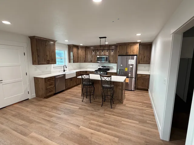 Kitchen with appliances with stainless steel finishes, light wood finished floors, decorative light fixtures, recessed lighting, and dark brown cabinets
