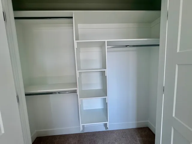 Built-in closet system featuring white shelving, multiple hanging rods, and an integrated shelf unit