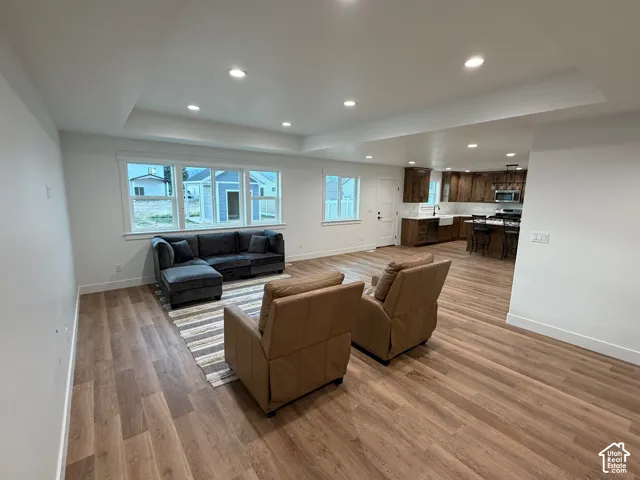 Living room with a raised ceiling, recessed lighting, and light wood-style floors