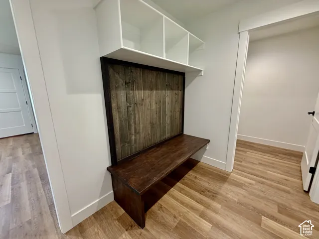 Built-in mudroom bench featuring a dark wood-finish seat, a rustic wood-finish back panel, and overhead white shelving