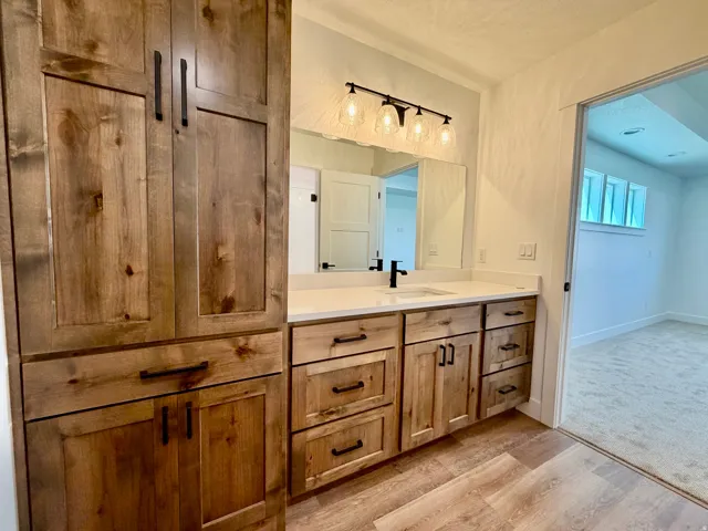 Bathroom vanity featuring wood-finish cabinetry, a white countertop, and a single basin sink with a black faucet