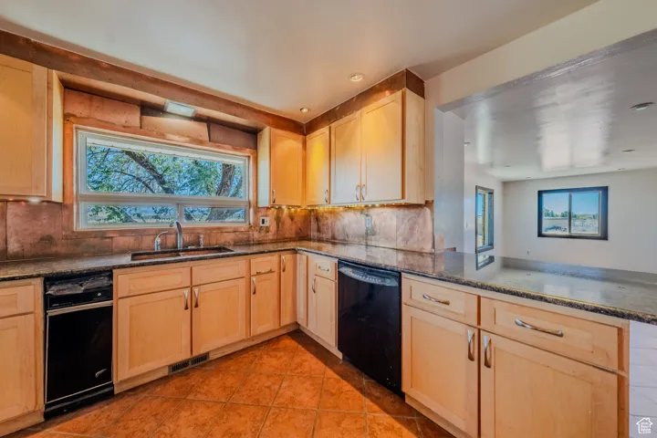 Kitchen with light brown cabinets, a peninsula, black dishwasher, dark stone counters, and recessed lighting