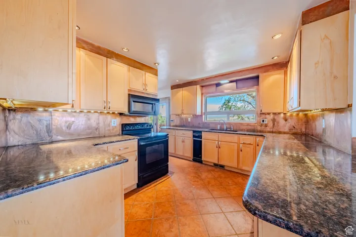 Kitchen with light brown cabinets, black appliances, dark stone countertops, recessed lighting, and backsplash