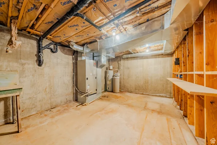 Unfinished below grade area featuring heating unit, water heater, and a water softener system