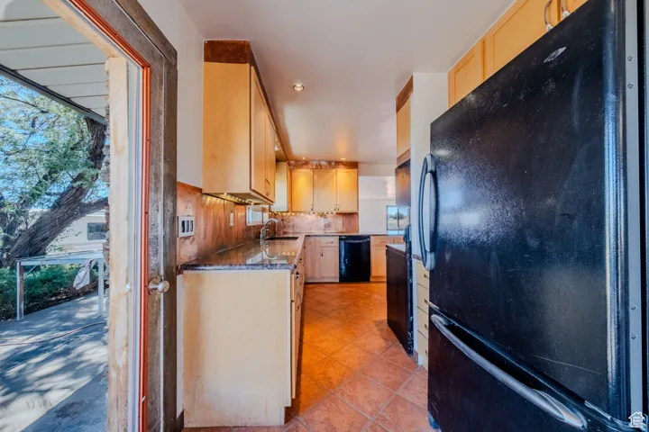 Kitchen featuring black appliances, light brown cabinetry, decorative backsplash, light tile patterned flooring, and dark stone countertops