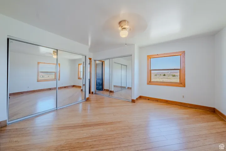 Unfurnished bedroom with light wood-style flooring, a ceiling fan, and multiple closets