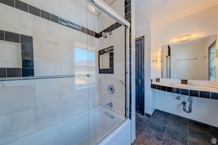 Bathroom featuring bath / shower combo with glass door and stone finish floors