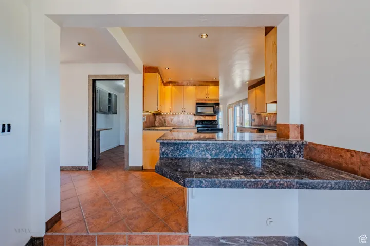 Kitchen featuring recessed lighting, black appliances, a peninsula, tasteful backsplash, and tile patterned floors