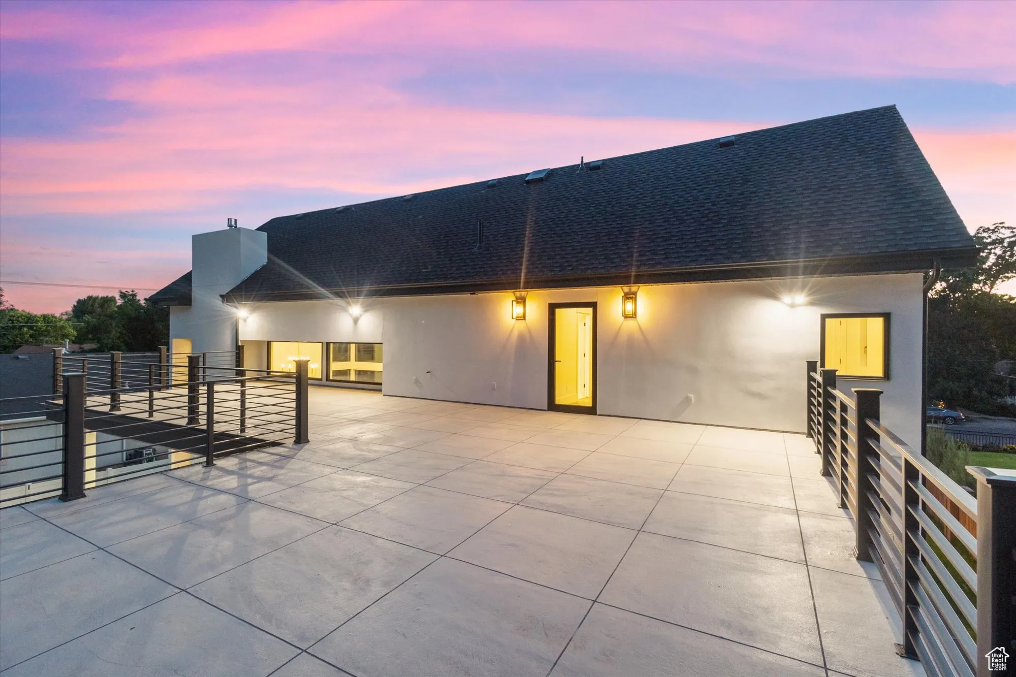 Rear view of property featuring a shingled roof, stucco siding, and a patio