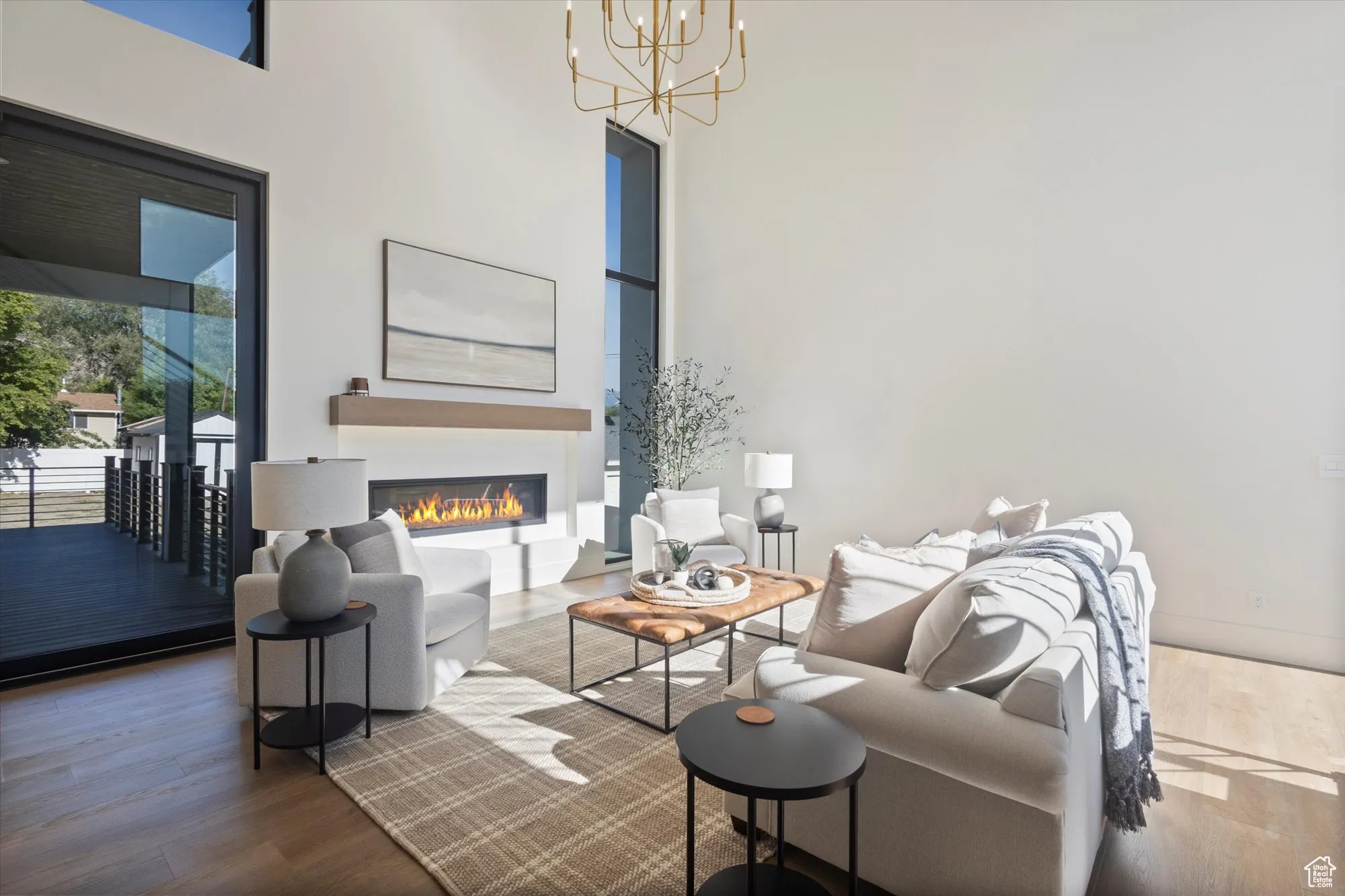 Living area with a towering ceiling, wood finished floors, a chandelier, and a glass covered fireplace