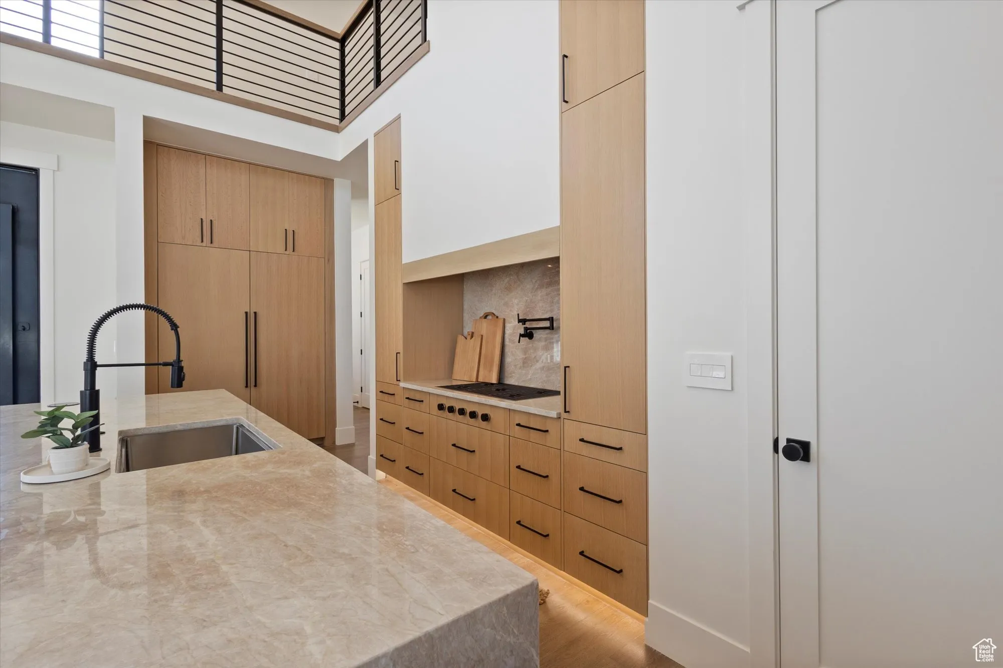 Kitchen featuring modern cabinets, light brown cabinetry, a high ceiling, light stone countertops, and light wood-type flooring