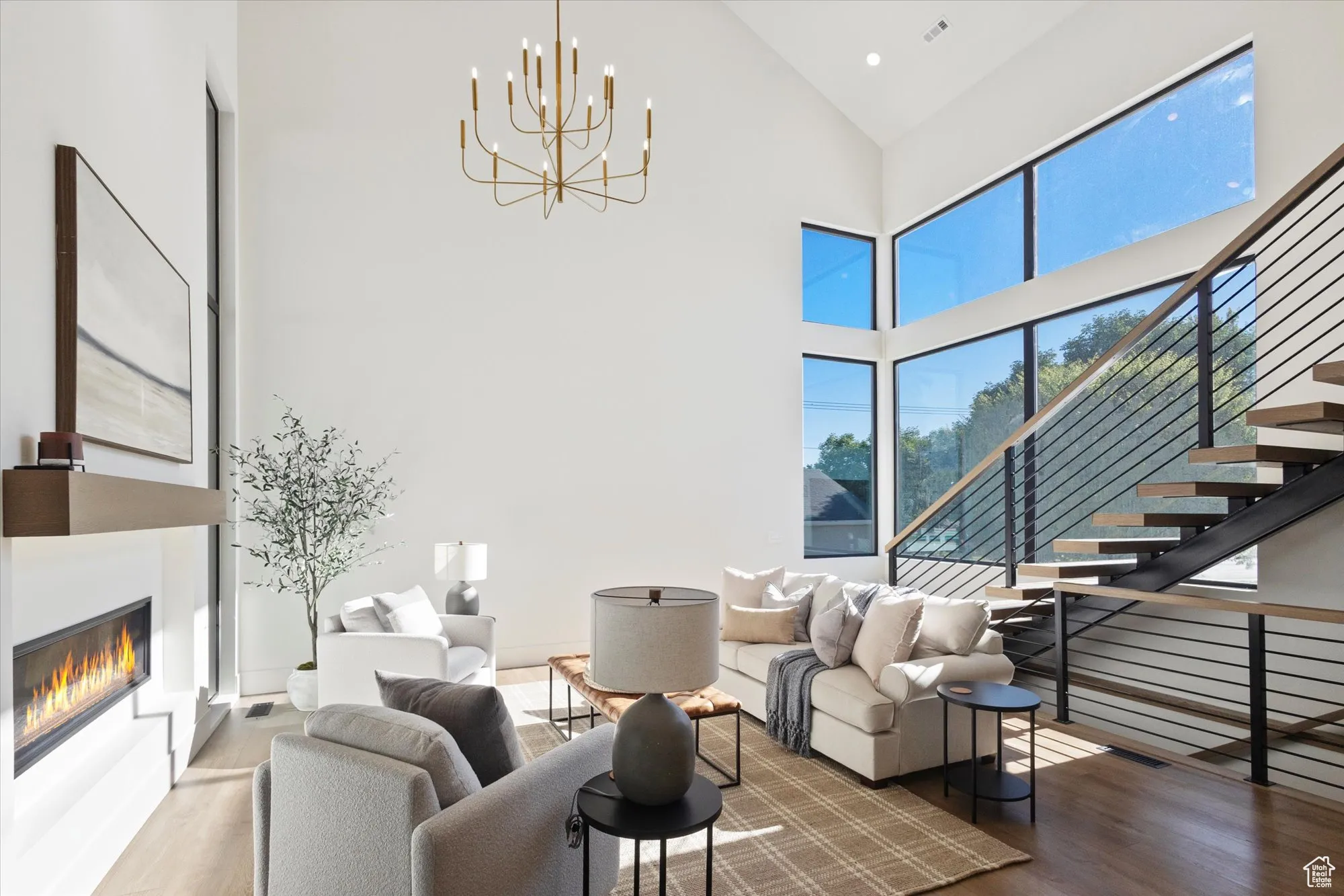 Living room featuring wood finished floors, high vaulted ceiling, a chandelier, and a glass covered fireplace