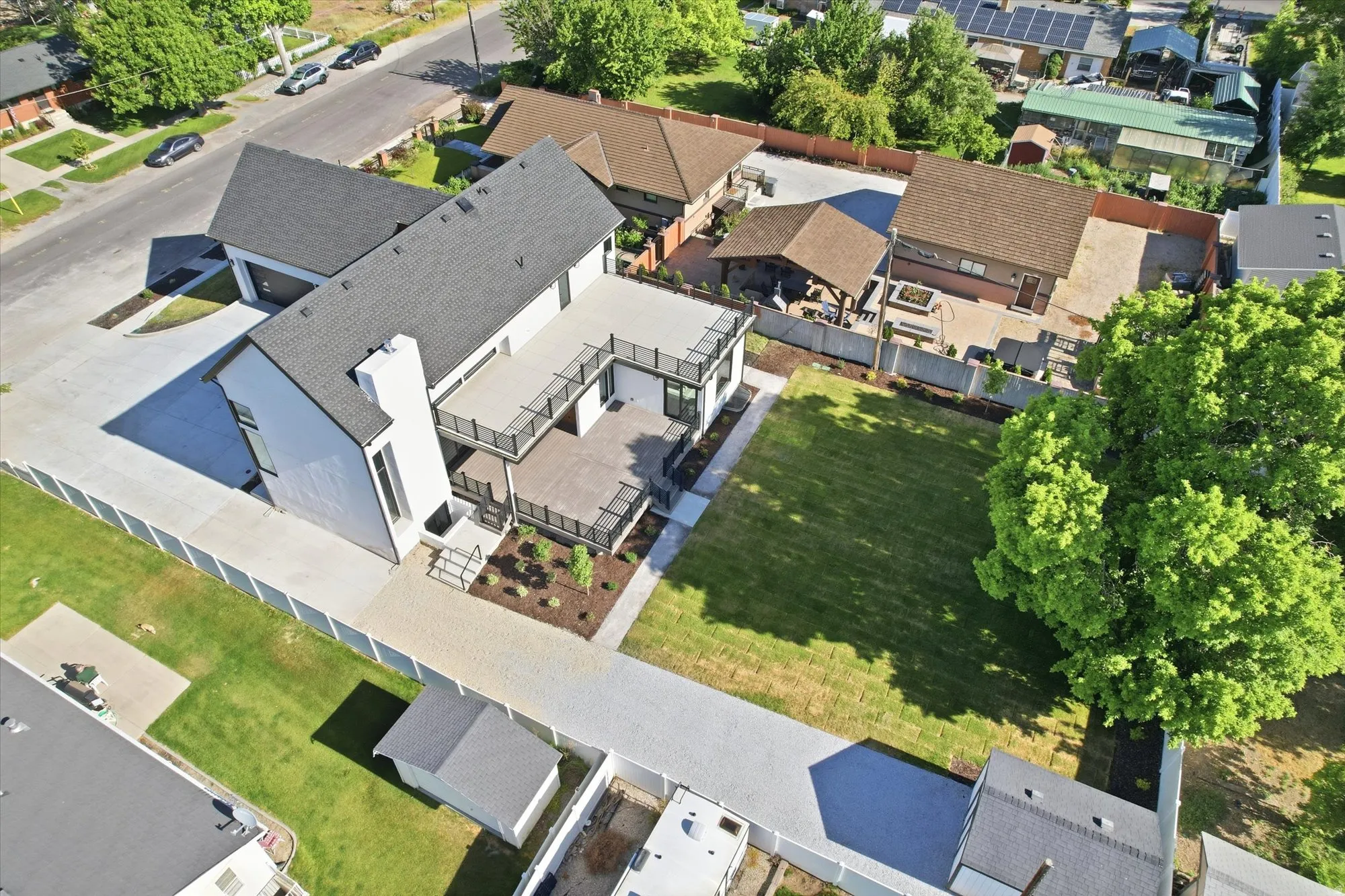 Modern exterior featuring white siding, a dark roof, a multi-level deck, a spacious paved patio, and a manicured lawn