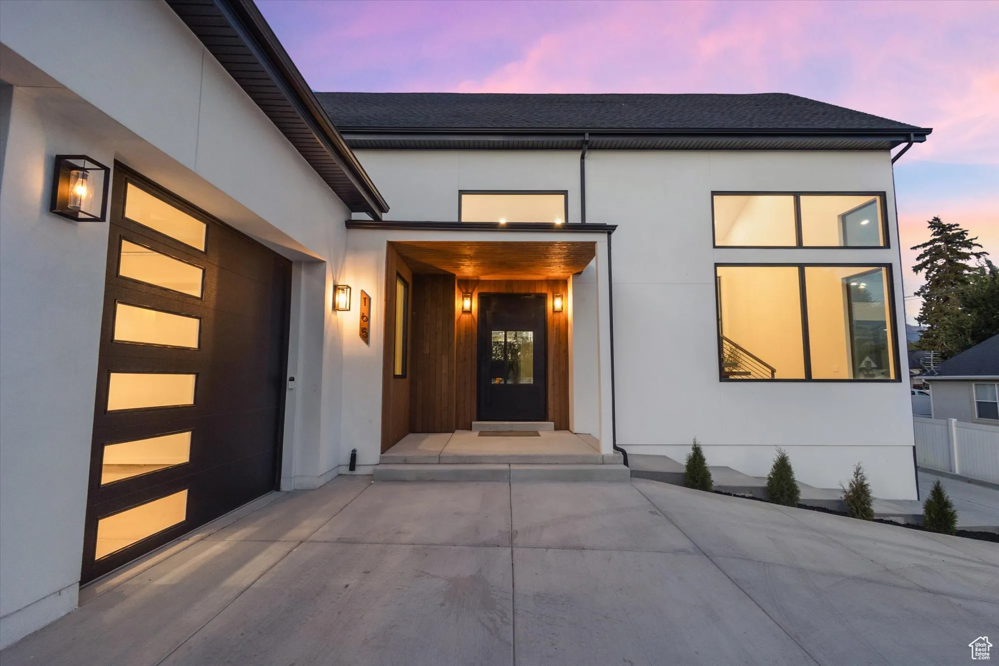 Exterior entry at dusk with stucco siding, roof with shingles, a garage, and driveway